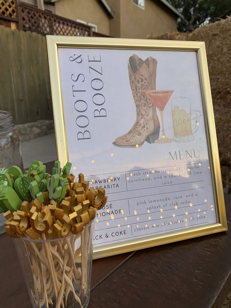 Gold-framed Boots & Booze drinks menu with a cowboy boot illustration beside cactus and horseshoe drink picks