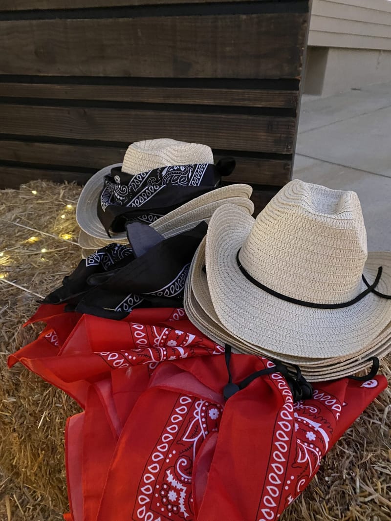 Straw cowboy hats with black and red bandanas piled on a hay bale
