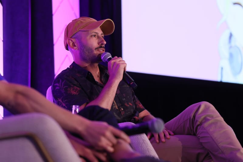 Speaker in an orange cap talking into a microphone from a cream armchair