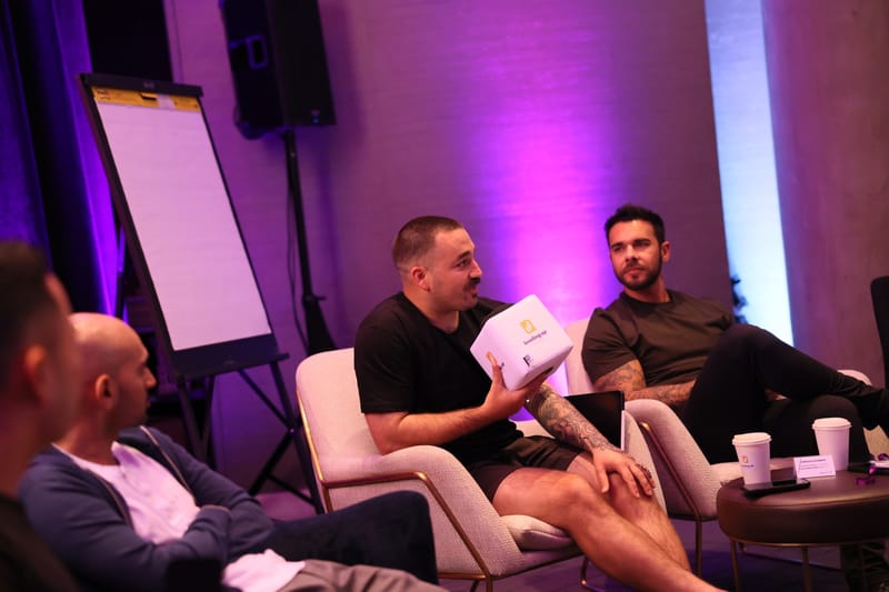 Three guests in cream armchairs beside a flip chart, one holding a cube microphone