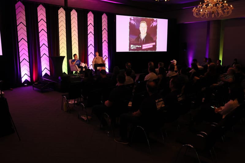 Packed session room facing a speaker on screen beside the lit chevron pillars