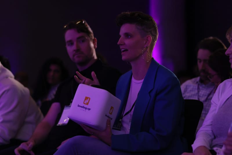 Guest in a blue blazer holding a Leveling Up cube microphone while talking in the audience