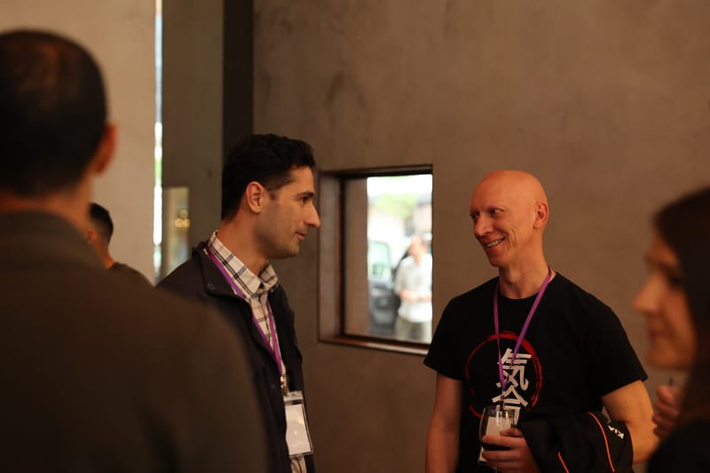 Two guests with lanyards talking during a break beside a concrete wall