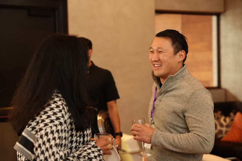 Guest in a grey sweater laughing with a drink in hand during networking