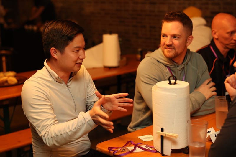 Guests talking at a long wooden table with a paper towel roll and purple lanyards