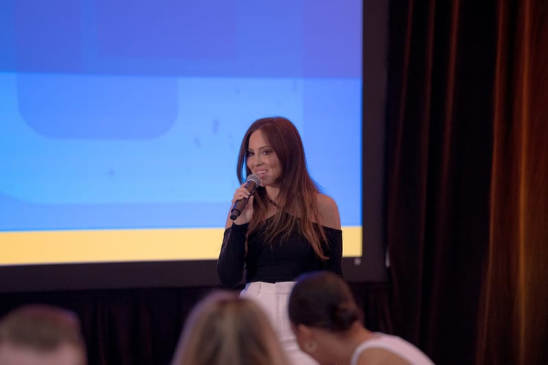 A speaker in a black top talking into a microphone in front of a blue screen
