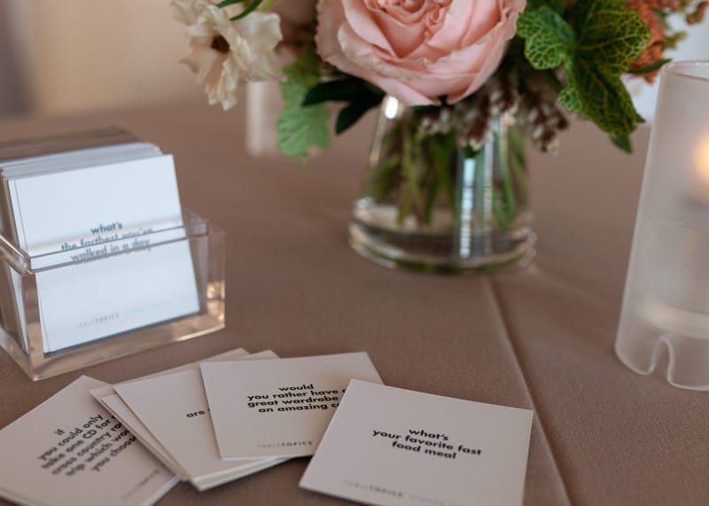 TableTopics conversation cards in a clear holder beside a vase with a pink rose