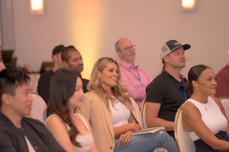 Guests smiling in the audience, one in a pink shirt wearing a lanyard