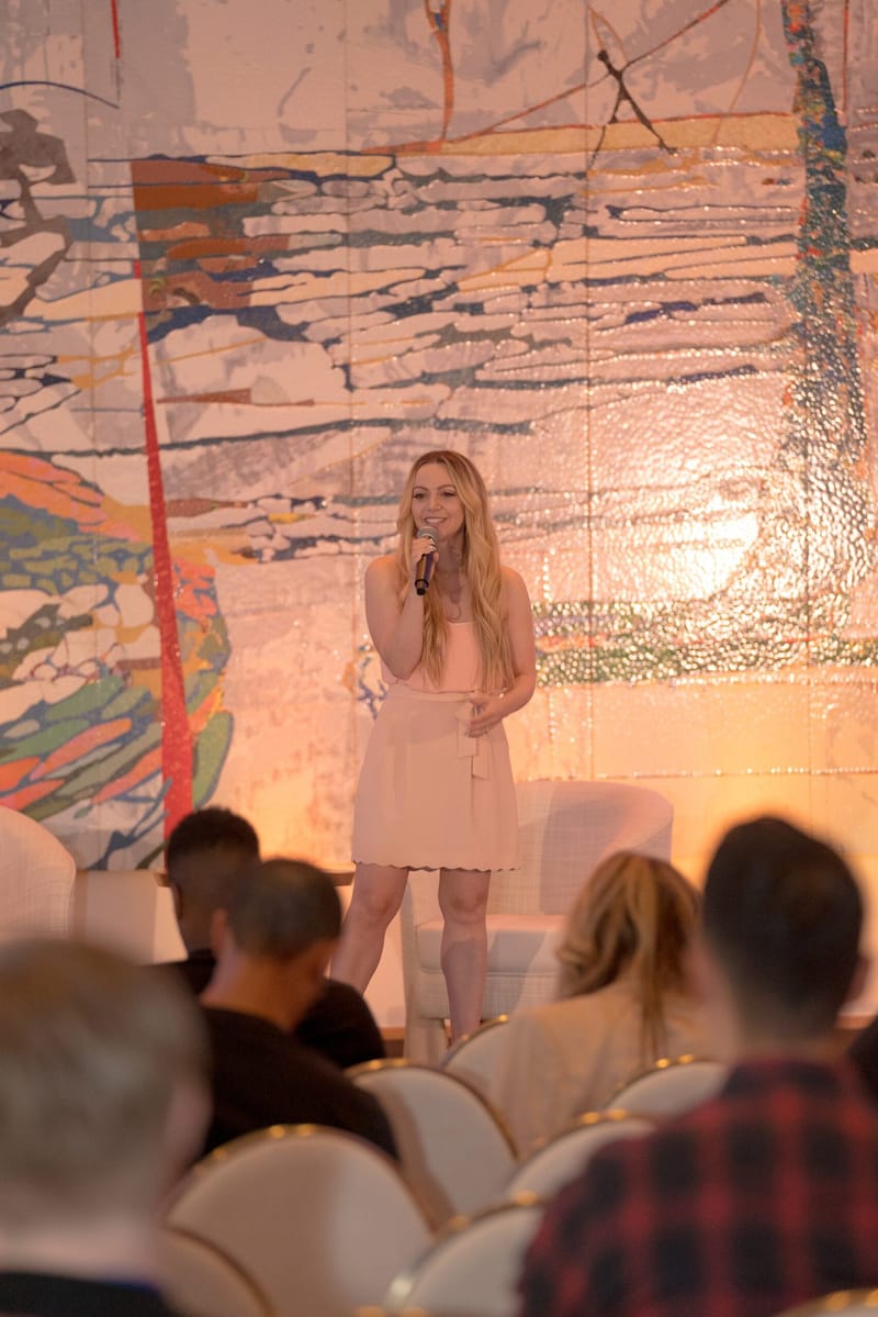 Speaker in a pale pink outfit holding a microphone in front of the painted wall