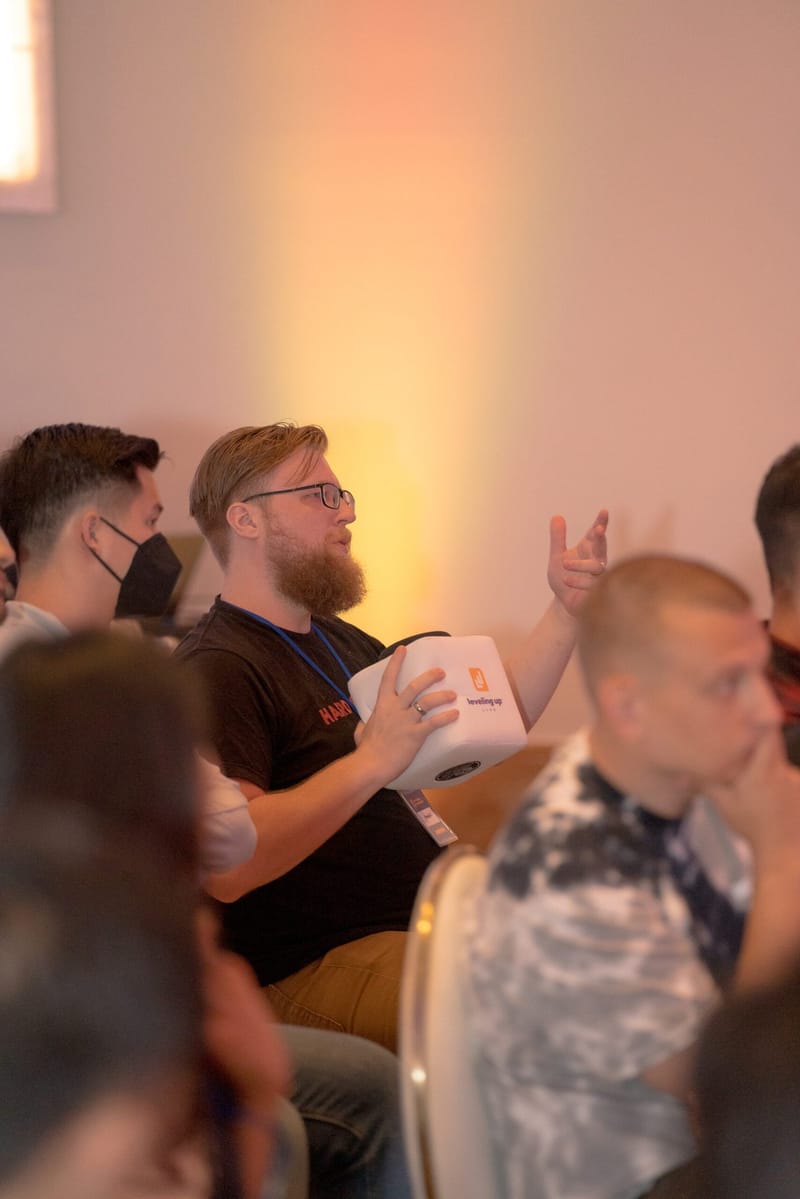 Guest holding a white cube microphone and gesturing while asking a question