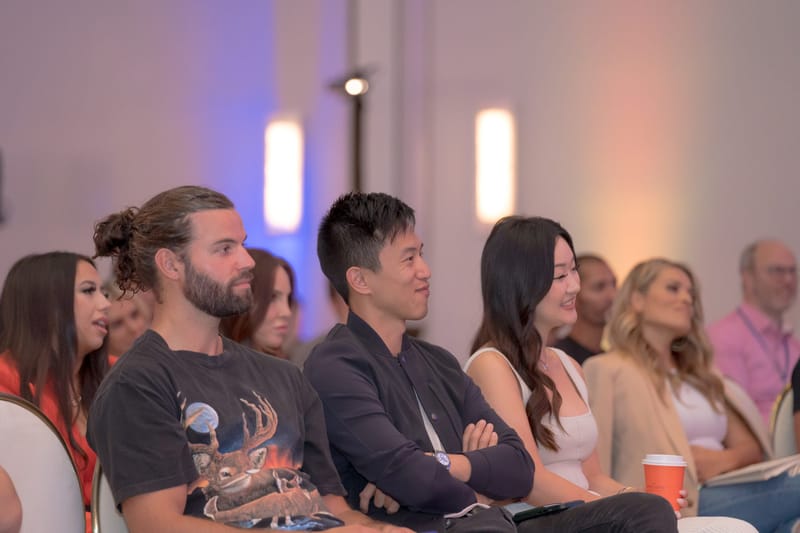 Row of guests listening and smiling, one holding an orange cup