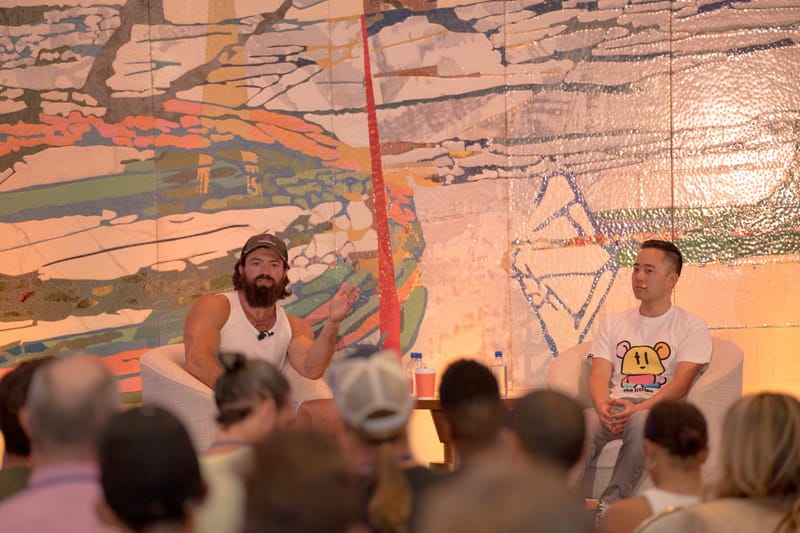 Two speakers in armchairs talking in front of the painted wall as guests watch