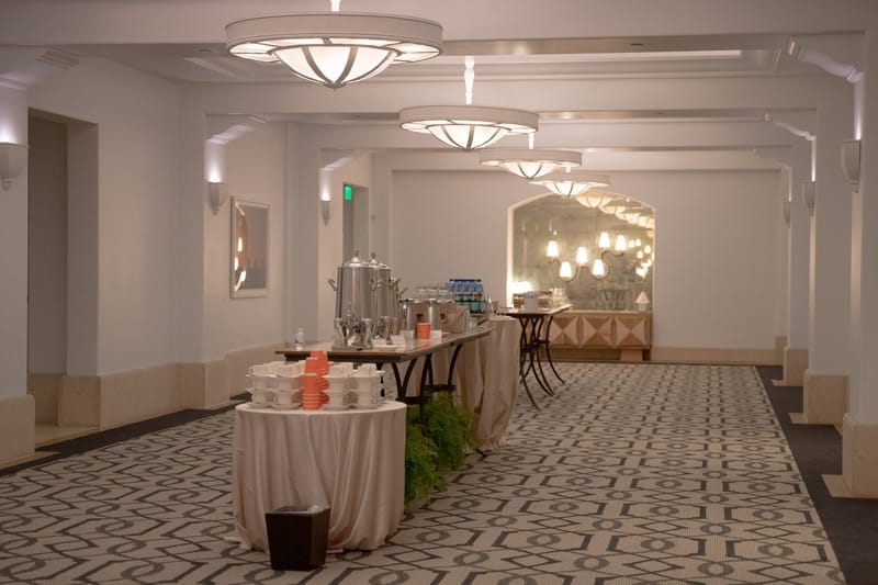 Hotel hallway with a coffee station and cups set on draped round tables