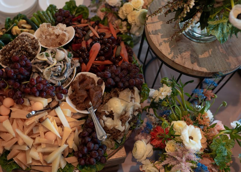 Grazing board of cheese, grapes, carrots and dried fruit beside fresh flowers