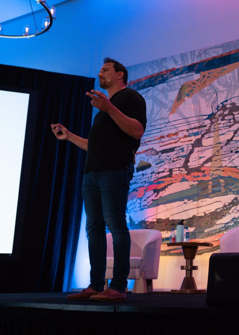 Speaker in a black T-shirt gesturing on stage in front of the painted wall