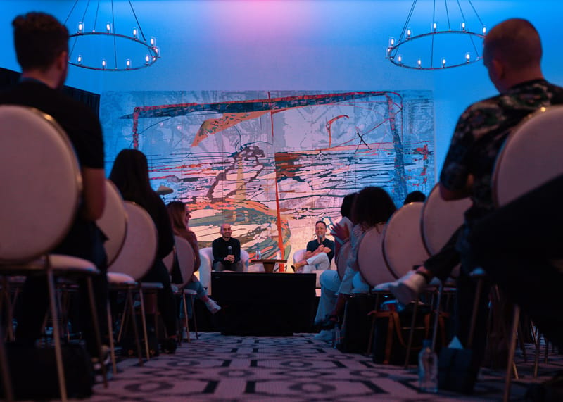 View down the aisle between guests to two speakers in armchairs on stage