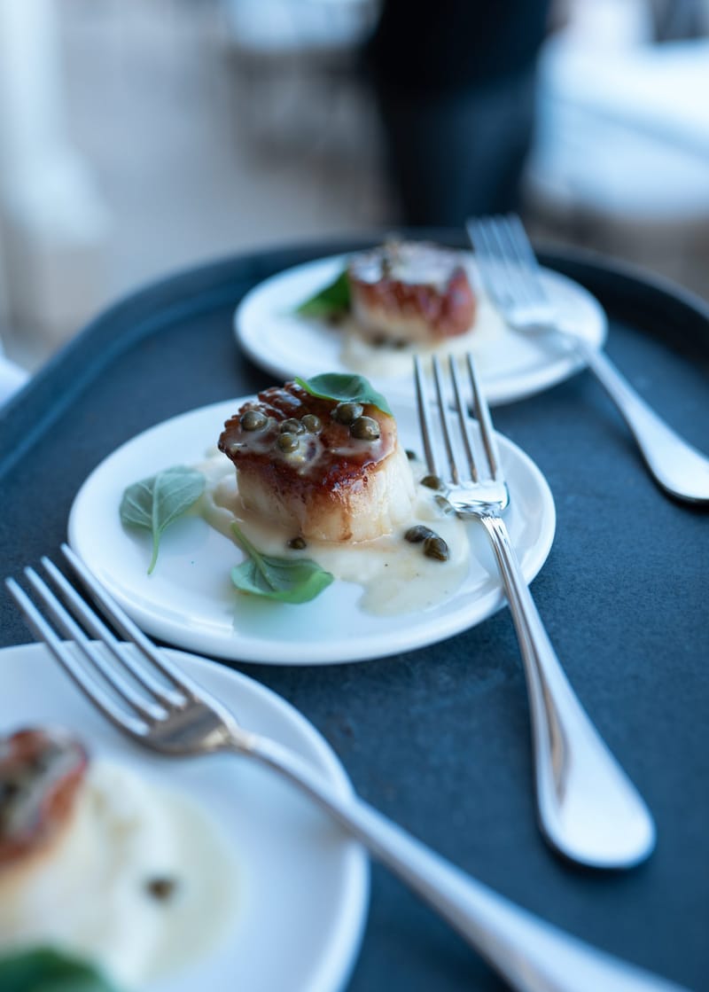 Seared scallops with capers and basil on small plates next to silver forks