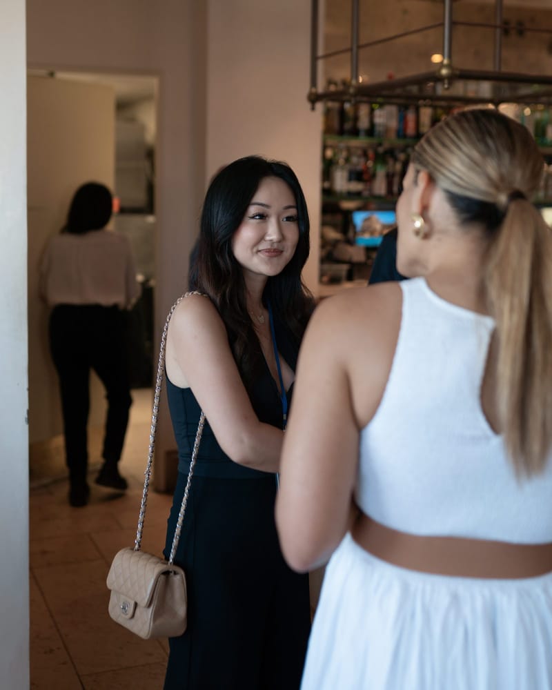 Two guests talking indoors, one carrying a quilted handbag