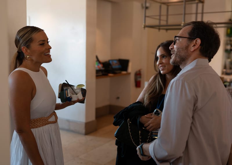 Three guests chatting and laughing, one in a white dress holding a drink