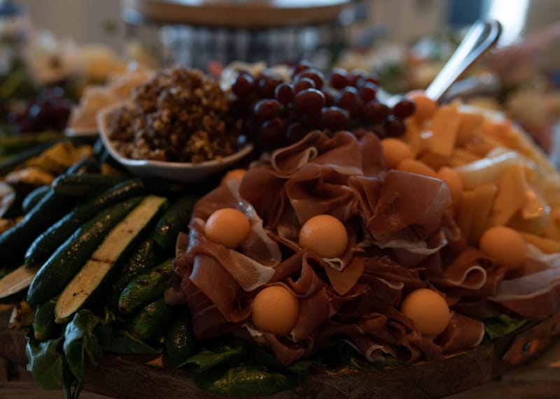 Close view of cured meat, melon balls, cheese, grapes and grilled zucchini on a grazing board