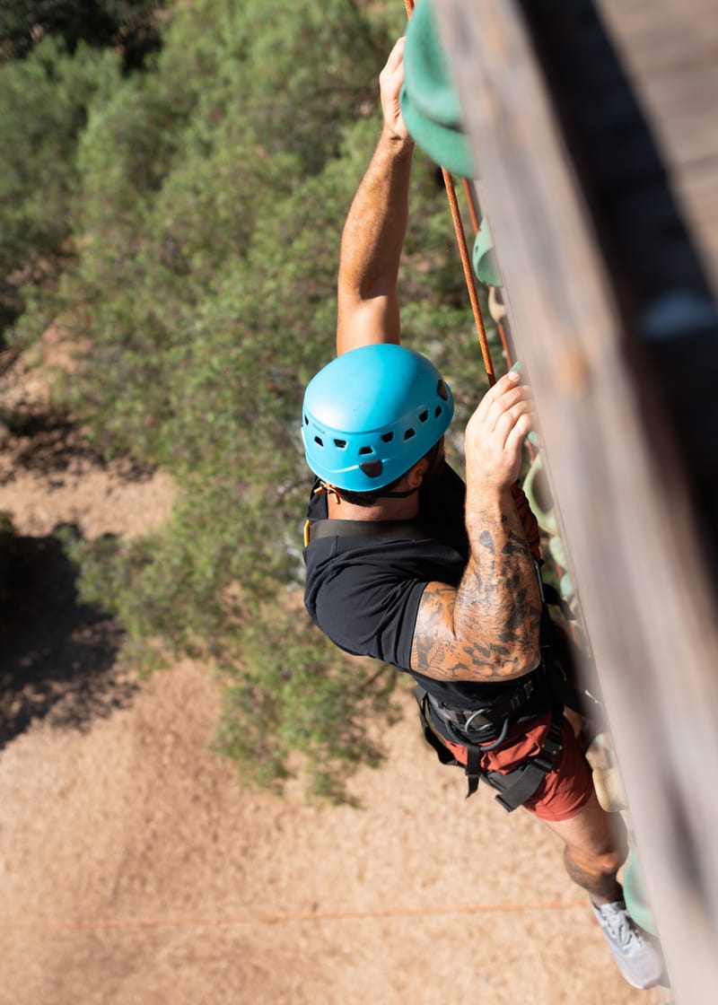Guest in a blue helmet reaching for handholds on a wooden pole, seen from above