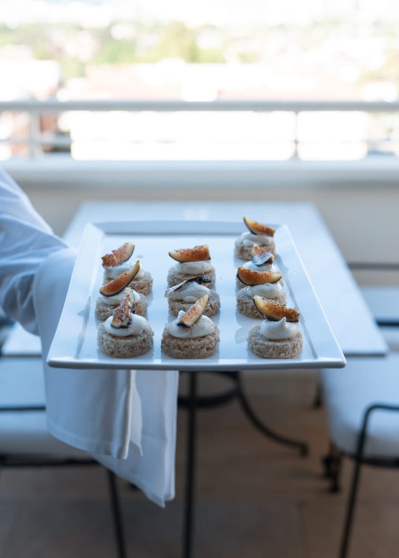 Tray of small canapes topped with fig slices held on a terrace