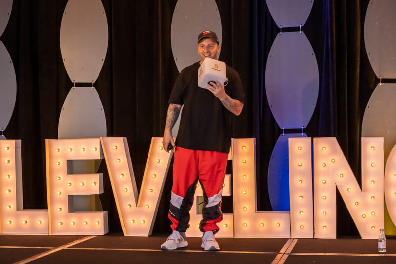 Speaker in a black cap holding a white Leveling Up cube microphone in front of marquee letters