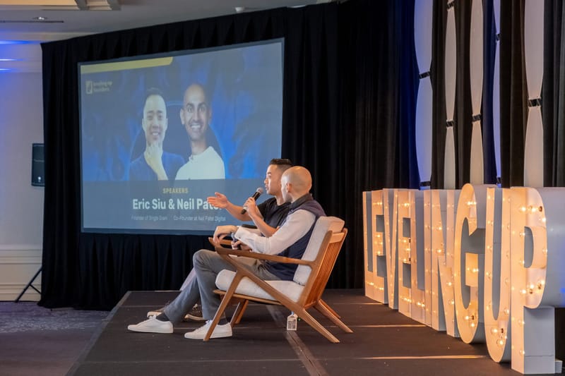 Two speakers in wooden armchairs under a screen reading Speakers, Eric Siu & Neil Patel