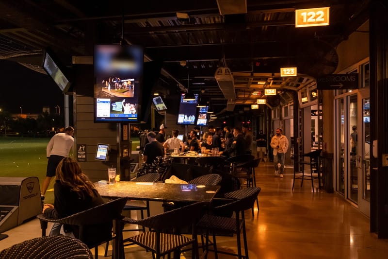 Guests at tables along the lit Topgolf bays, with leaderboard screens hanging overhead