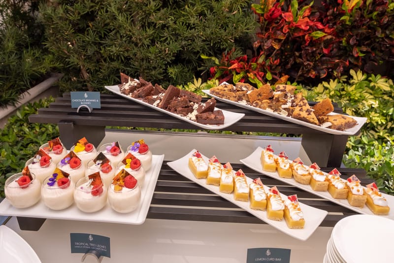 Tropical tres leches cups, lemon curd bars, brownies and blondies on a tiered stand among plants