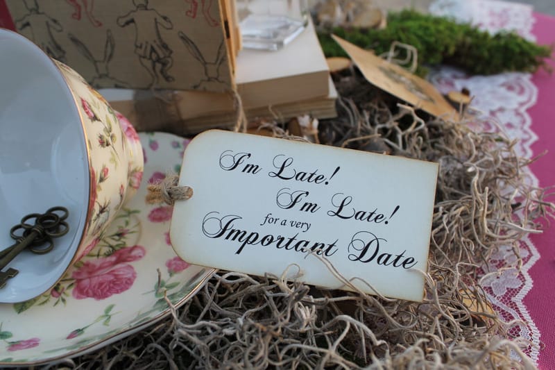 Tag reading I'm Late! I'm Late! for a very Important Date beside a floral teacup and an old key