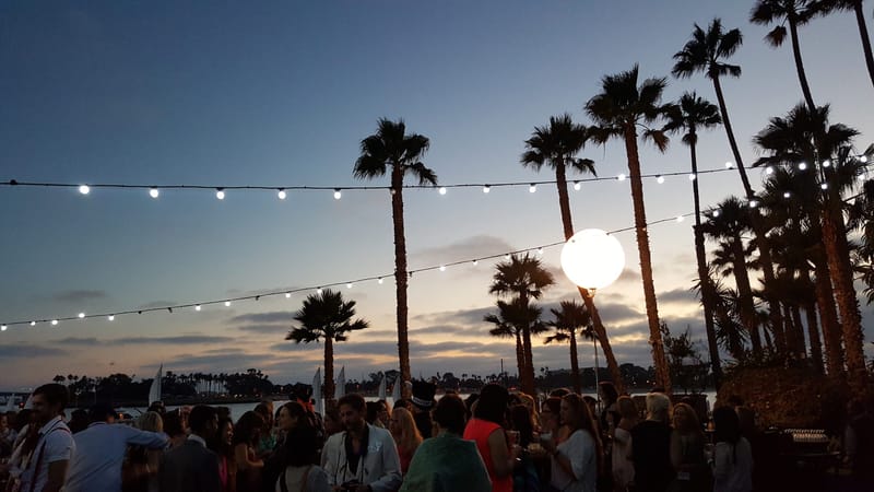 Guests gathered under string lights and a glowing globe light among palm trees at dusk