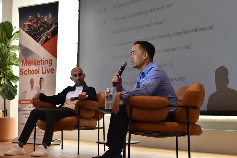 Two speakers talking in orange lounge chairs before a screen of questions and a Marketing School Live banner
