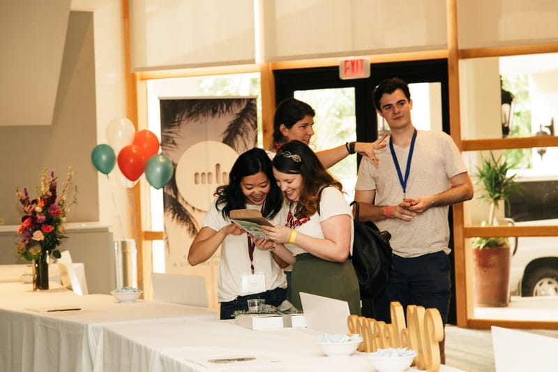 Guests looking through a booklet at a check-in table with flowers, balloons and a palm print banner