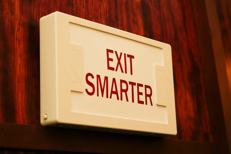 Sign styled like an exit sign reading EXIT SMARTER on a wood-paneled wall