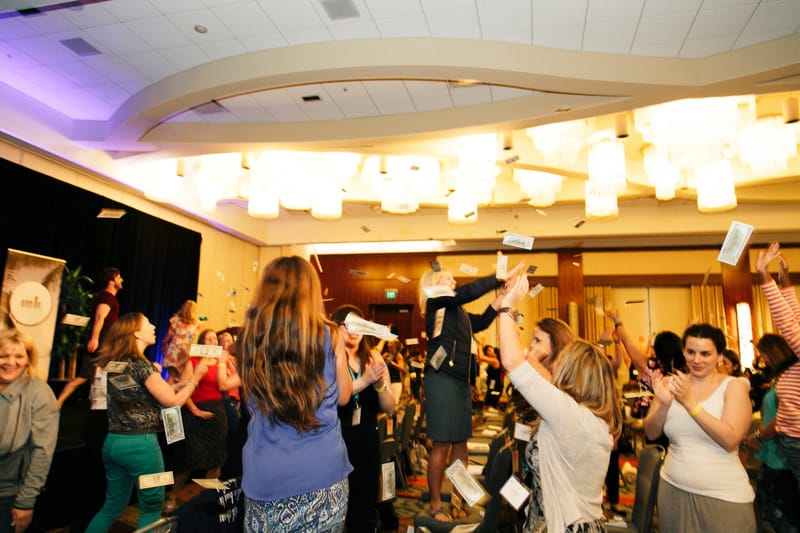 Guests in a room with chandeliers throwing papers into the air