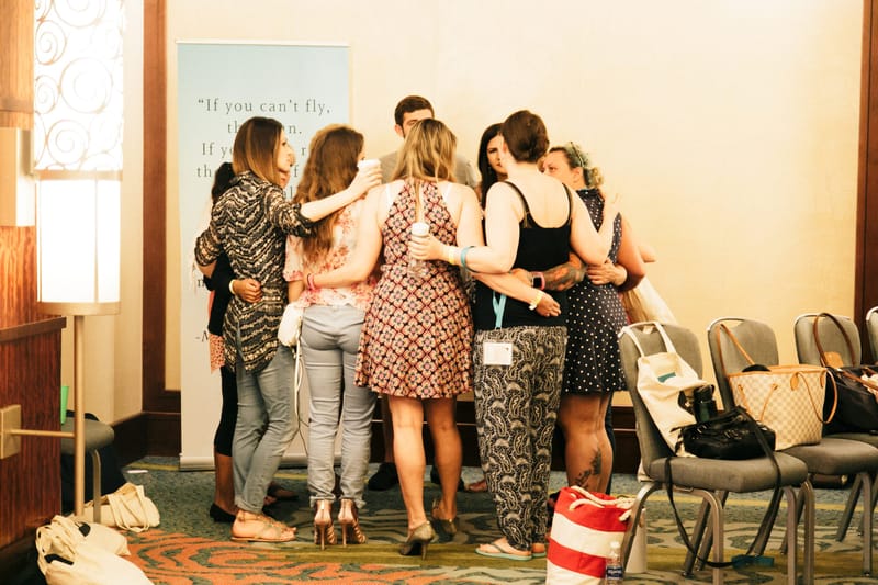 A group of guests hugging beside a banner that begins If you can't fly