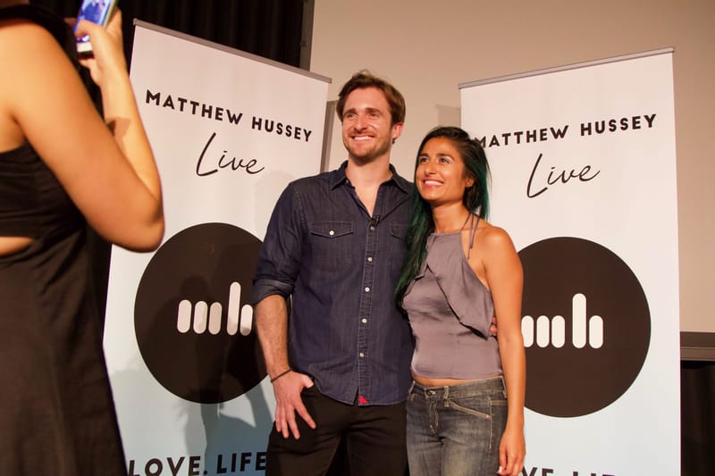 A man and a guest posing for a phone photo between two Matthew Hussey Live banners