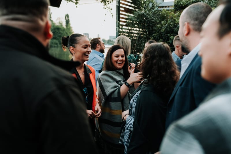 Guests laughing and talking together in a close group outdoors among trees