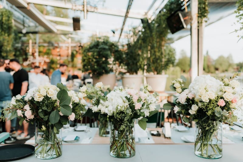 Three glass vases of white hydrangeas, pale pink roses and eucalyptus in front of mingling guests