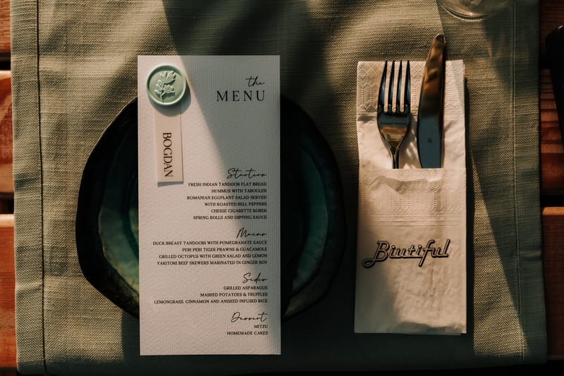 Menu card with a pale green wax seal and a name tab beside cutlery tucked in a Biutiful napkin
