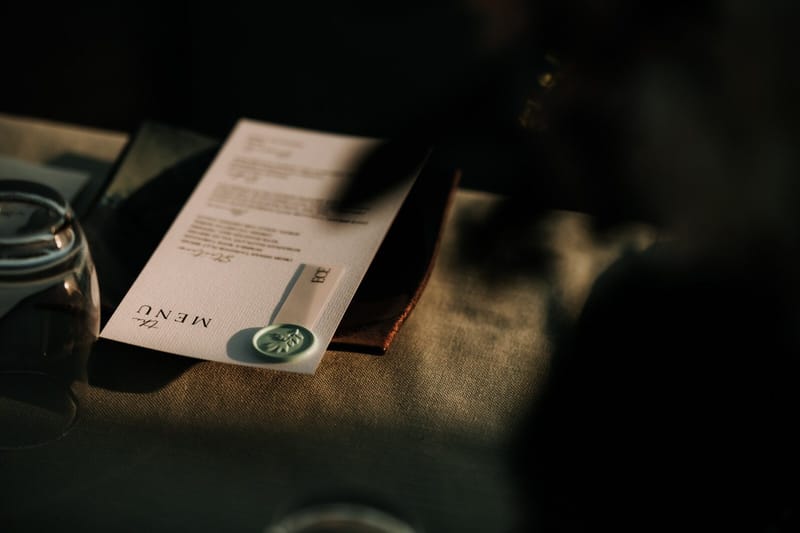 Menu card with a pale green wax seal lying in low evening light and shadow
