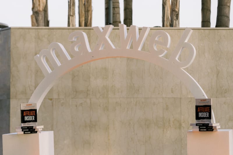 Arched white maxweb letter sign against a stone wall, with Affiliate Insider books on white plinths either side