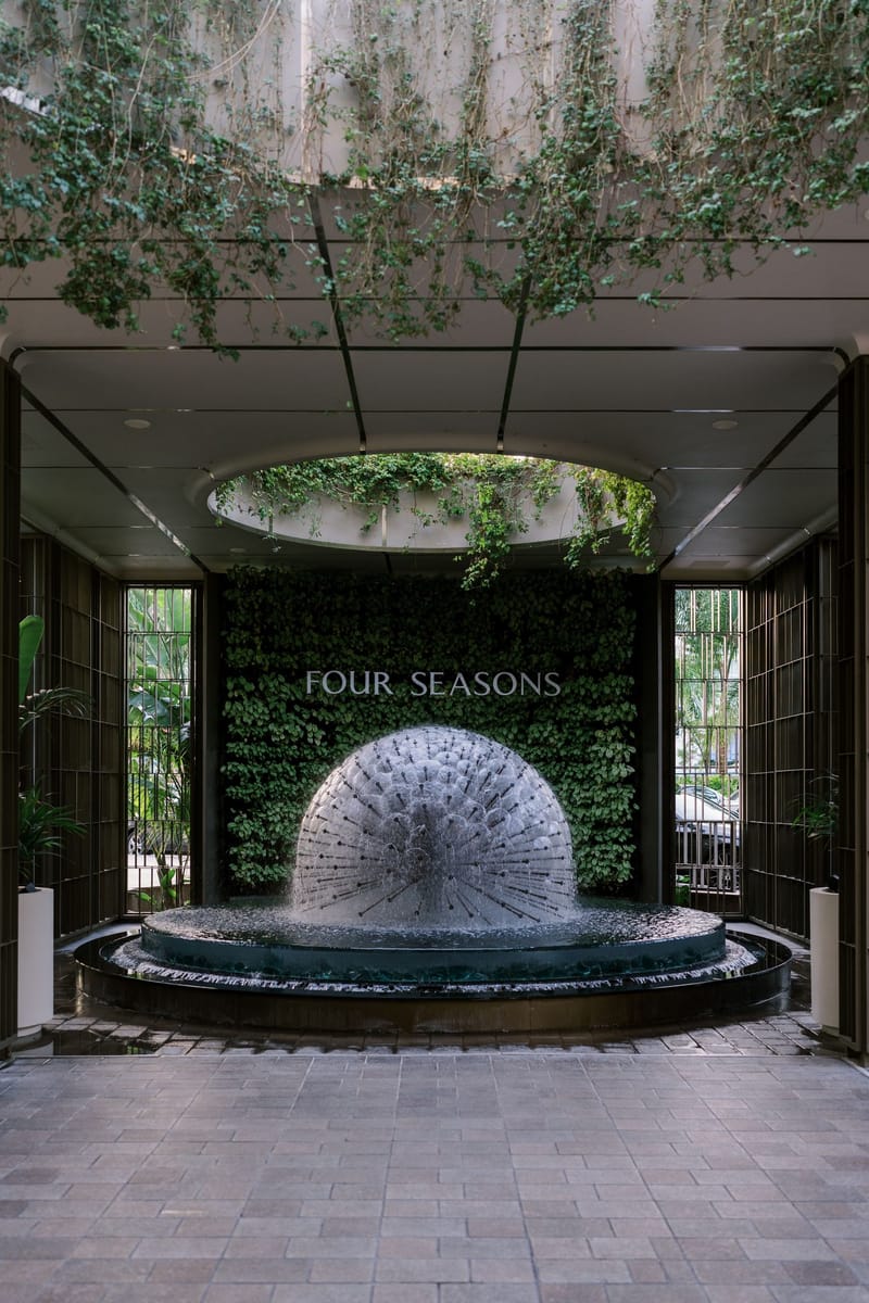 FOUR SEASONS lettering on a green plant wall behind a round dome fountain at an open entrance