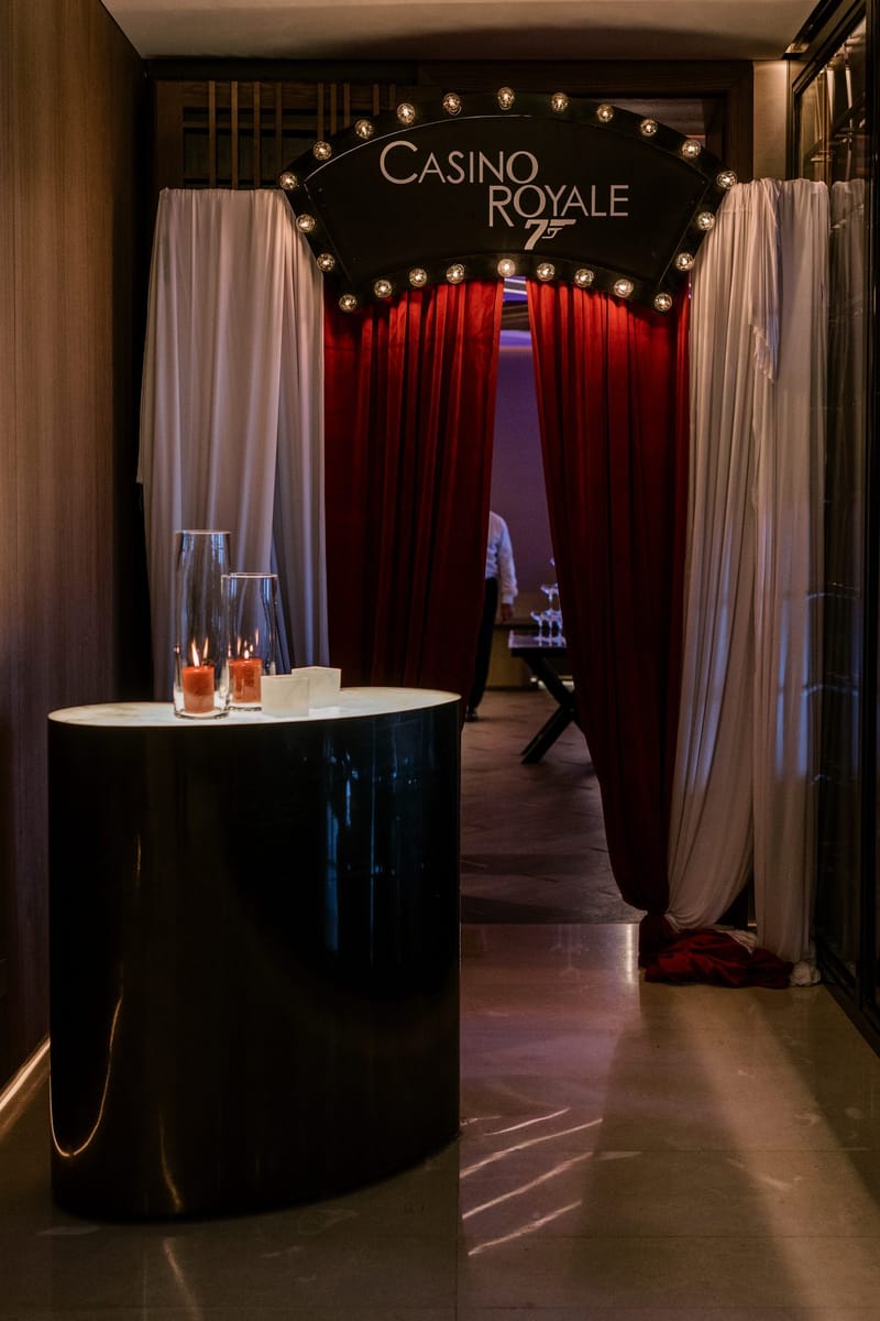 Lit CASINO ROYALE marquee sign above red velvet curtains and white drapes, with candles on a side table
