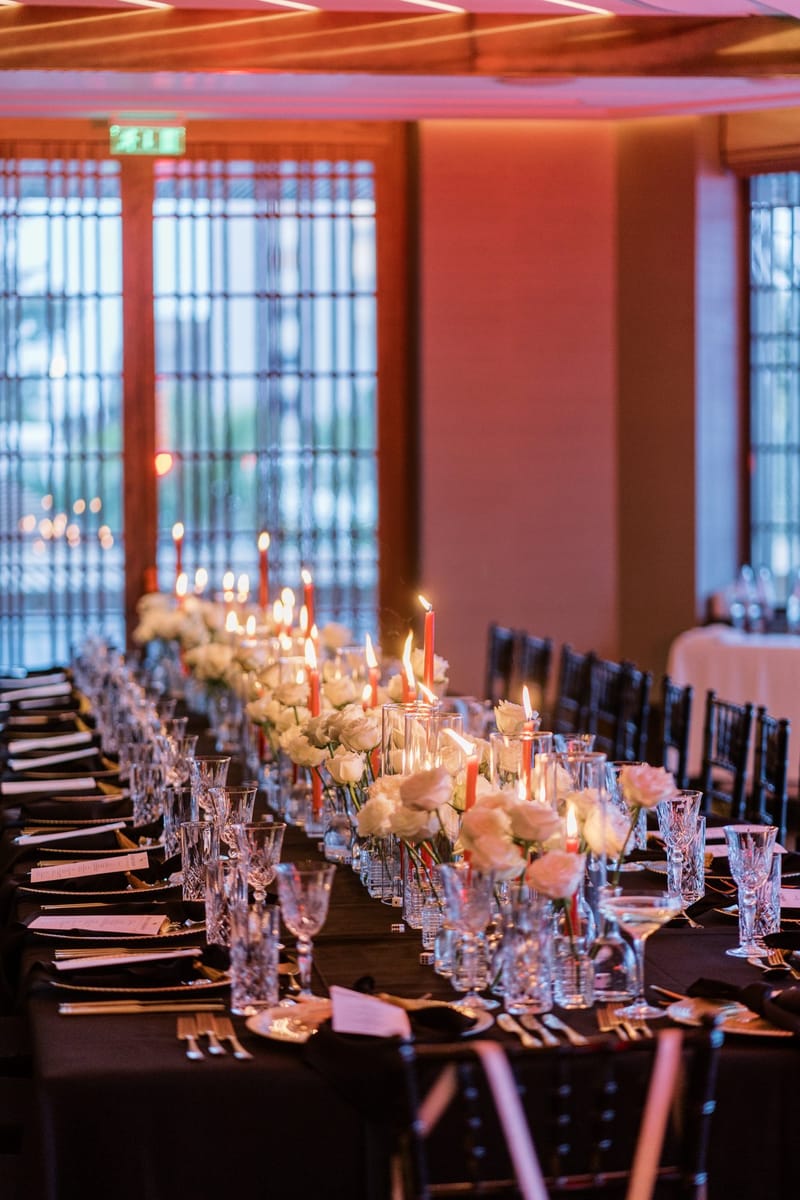 Long dinner table with black cloths, tall candles, white roses and rows of crystal glasses