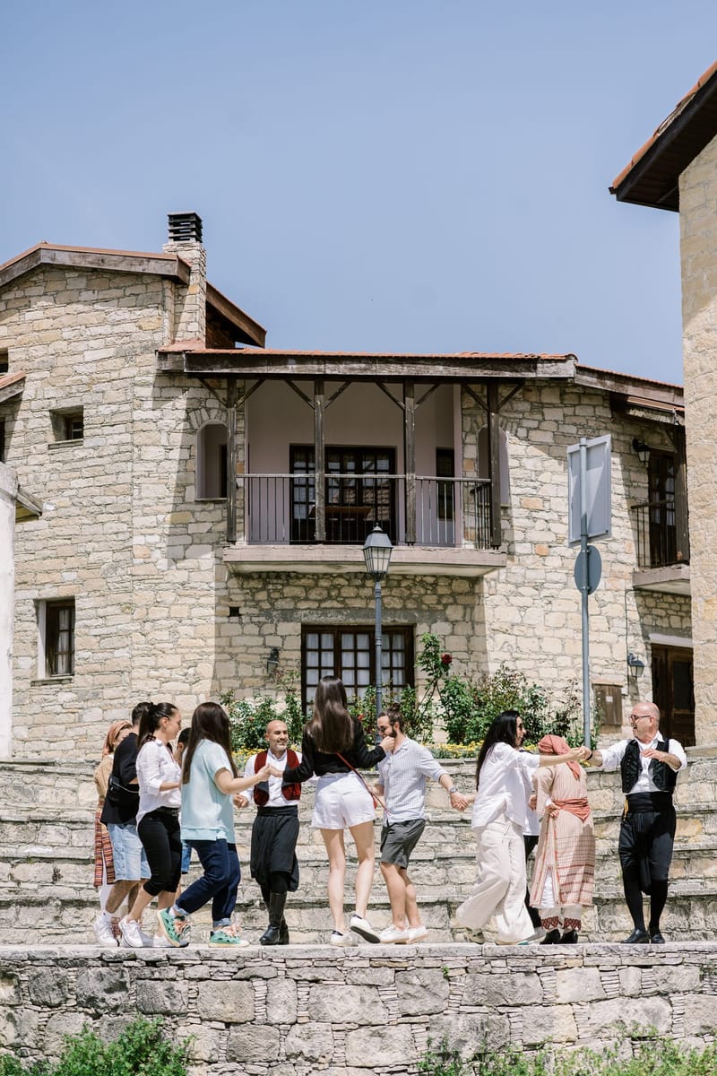 Guests dancing arm in arm with performers in traditional dress outside a stone building