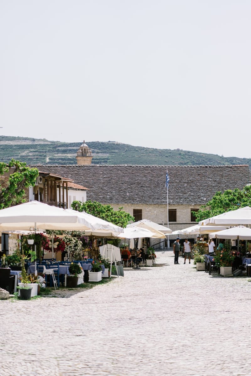 Cobbled street lined with white umbrellas and cafe tables, a bell tower on the hill behind
