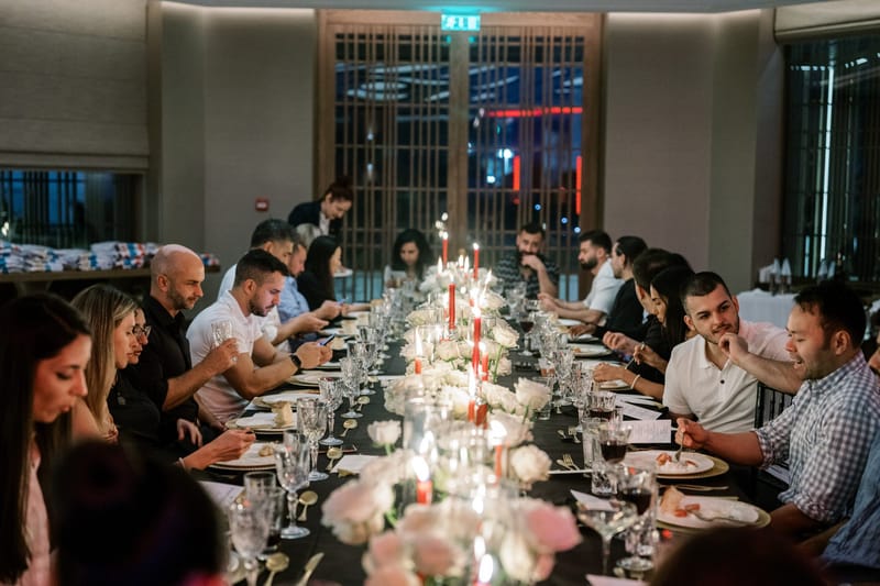 Guests dining along a candlelit table with pink and white roses and red taper candles