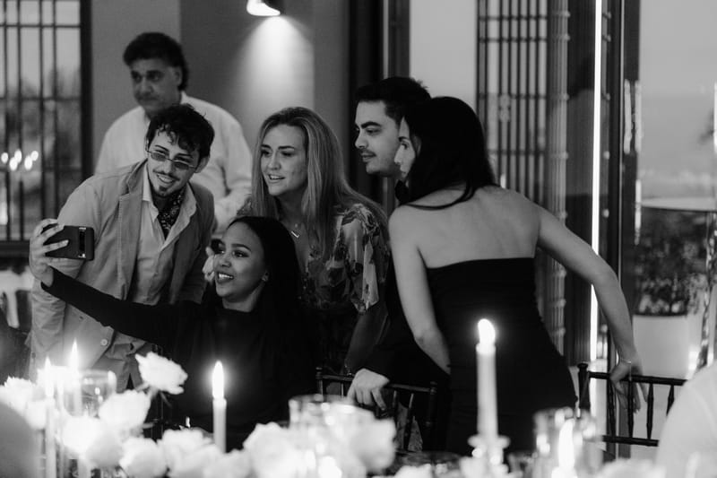 Black and white photo of guests taking a selfie at a candlelit dinner table